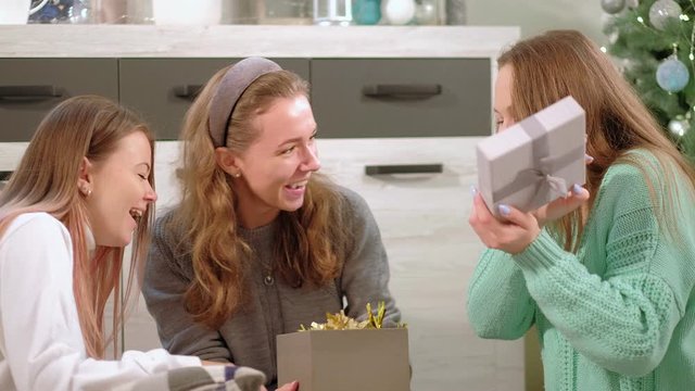 Christmas present. Home celebration. Happy female friends opening gifts at home.