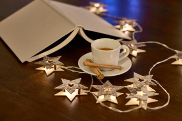 Una taza de café con canela, rodeada de un libro y luces navideñas en forma de estrellas