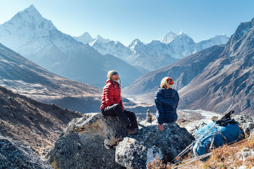 Cute Couple resting on the Everest Base Camp trekking route near Dughla 4620m. Man and woman enjoying a rest.They left Backpacks and trekking poles and enjoying valley view with Ama Dablam 6812m peak - obrazy, fototapety, plakaty