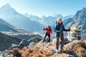 Couple following Everest Base Camp trekking route near Dughla 4620m. Backpackers carrying Backpacks and using trekking poles and enjoying valley view with Ama Dablam 6812m peak - obrazy, fototapety, plakaty