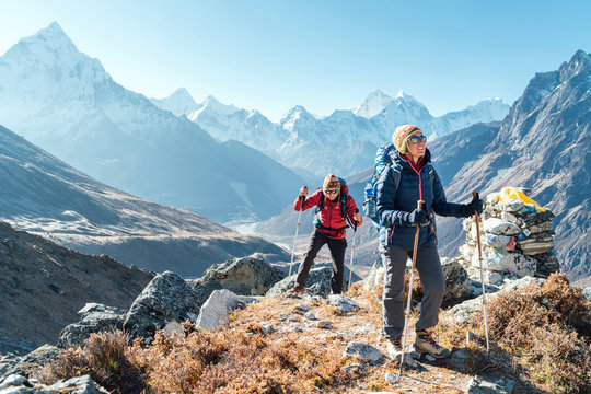 Couple following Everest Base Camp trekking route near Dughla 4620m. Backpackers carrying Backpacks and using trekking poles and enjoying valley view with Ama Dablam 6812m peak