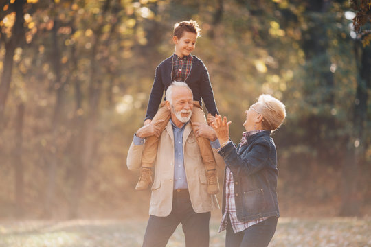 A wonderful day with their grandson. The grandparents are walking with their grandchild on his grandfather's shoulders, and the grandmom walking beside them, both showering the child with love.