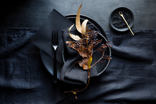 Dramatic table setting with black crockery, black paper stationery menu, linens, dark berries and black salt