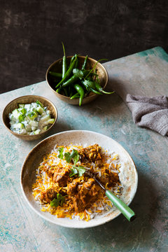 Table setting with a bowl of chicken curry with cucumber raita side dish