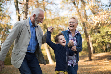 A grandfather, a grandmother and their grandson strolling through an outdoor environment full of...