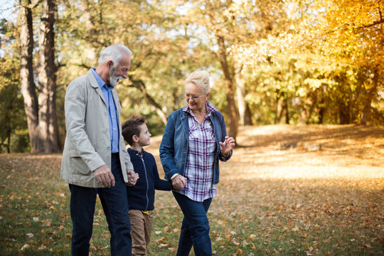 Grandparents and their grandson strolling through a park in an autumn afternoon.