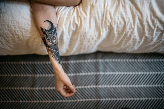 Hand with owl tattoo hanging out of bed
