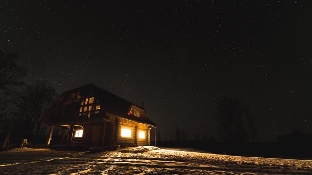 Time lapse of night sky with a log cabin in winter
