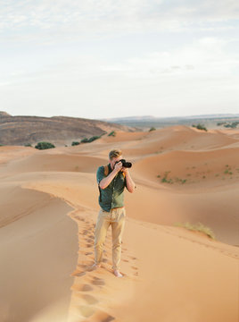 A European man in a desert taking a picture with a camera