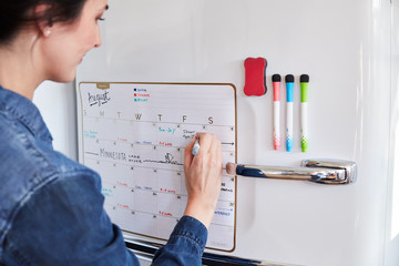 Woman filling out calendar on fridge
