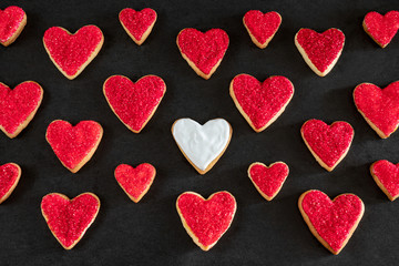 Red and white heart shaped cookies on black background, distinction concept, love symbol