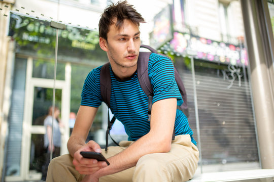 young man sitting at bus stop with cellphone in hand