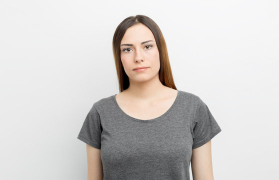 Portrait of a calm young woman in a gray t-shirt looking at the camera on a white background. Casual lifestyle and beauty concept.
