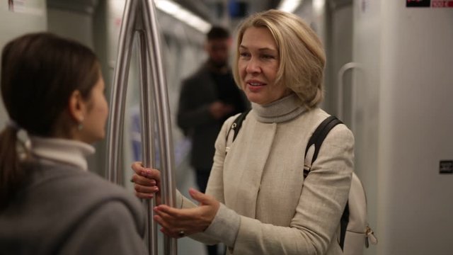 Portrait of mature woman talking friendly with her fellow traveler in modern subway car