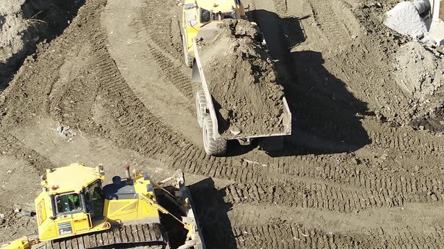 Aerial pullback shot of a dumper truck tipping earth in front of a bulldozer and roller.