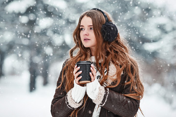 Fototapeta na wymiar Happy young woman with cup of coffee in snowy winter day. Girl enjoys winter, frosty day. Walk in winter forest.