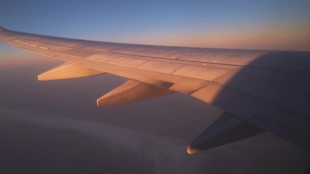  Wing of an airplane flying above the clouds at sunrise, view from the window of the plane