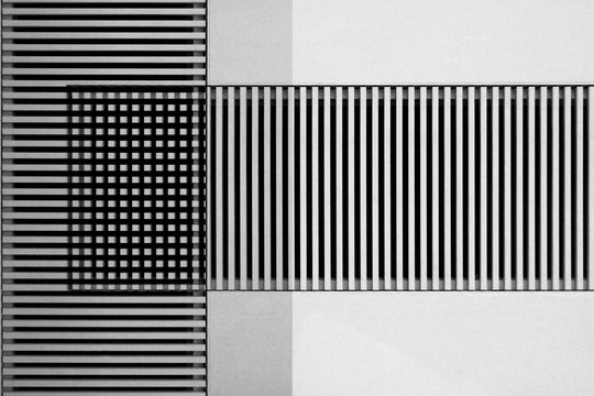 Lath structures viewed as regular stripes and checkers pattern in shades of gray. Business architecture background resembling bar codes against white stucco wall. Abstract geometric template.