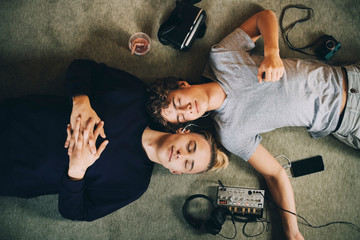 Directly above shot of male teenagers with closed eyes listening music while lying on carpet at home