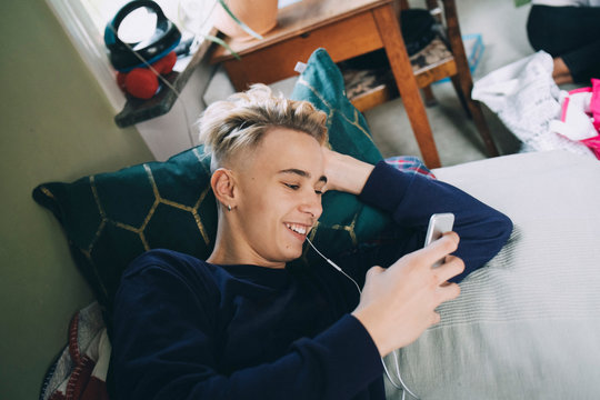 Smiling teenage boy text messaging on mobile phone at home