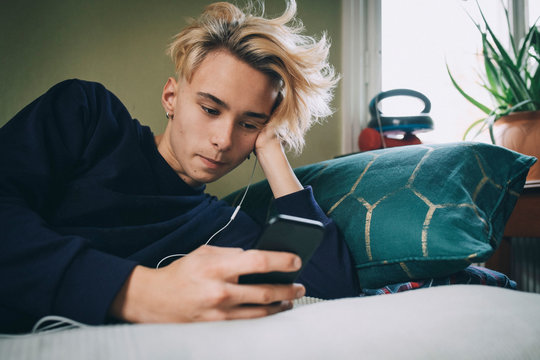 Teenage boy listening music while using mobile phone at bedroom