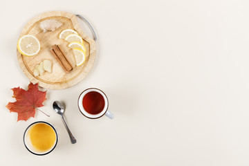 Lemon, ginger root and cinnamon sticks on wooden plate. Bowl of honey, cup of tea and maple leaf nearby. Natural remedies. Treatment of cold, flu and viruses at home. Healthcare concept. Copy space.