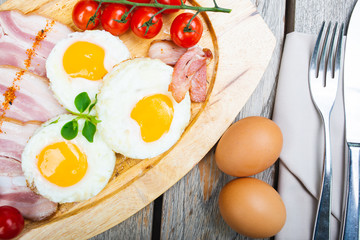 Tasty fried eggs with vegetables on a wooden plate.