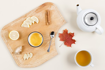 Slices of lemon, ginger, cinnamon sticks and bowl of honey on wooden plate. Teapot, cup of tea and maple leaf nearby. Flu season. Natural remedies. Treatment of cold and viruses. Healthcare concept.