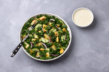 Kale gabage salad with baked potatoes, cucumber, red onions and mustard yogurt sauce on gray texture background