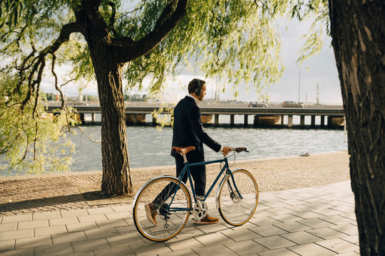 Businessman walking with bicycle on footpath in city