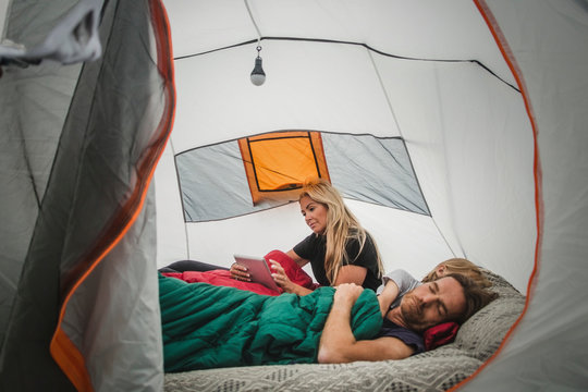 Woman using digital tablet while family sleeping in tent at campsite