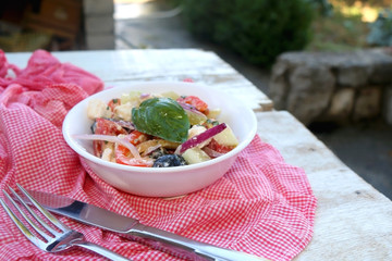 Fork, knife and bowl of Greek salad on a table outdoor. Selective focus.