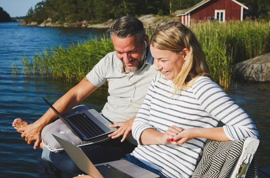 Smiling couple using laptop while sitting on bench by lake