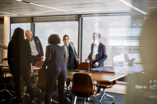 Smiling male and female lawyers shaking hands while greeting each other at board room in office