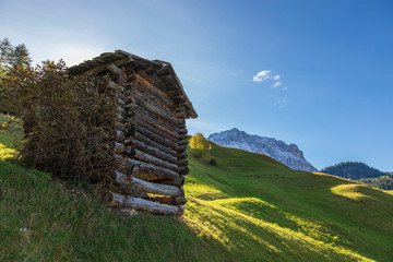 Wooden hayloft construction on green pastures and mountains with blue sky in background.