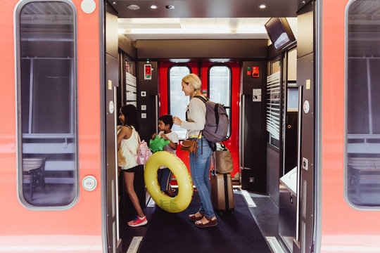 Mother and children with luggage walking in train at station - Powered by Adobe