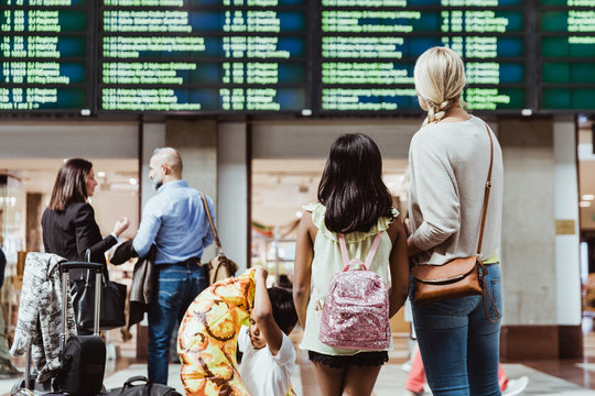 Family and business colleagues looking at arrival departure board while waiting in station - Powered by Adobe