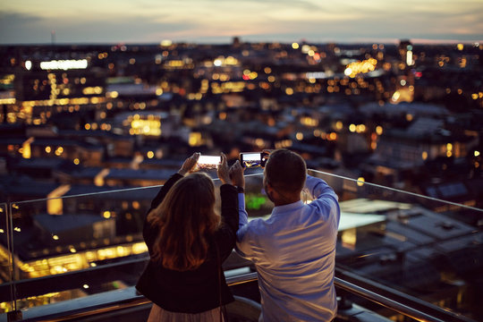 Rear view of businessman and businesswoman taking picture of city on smartphone