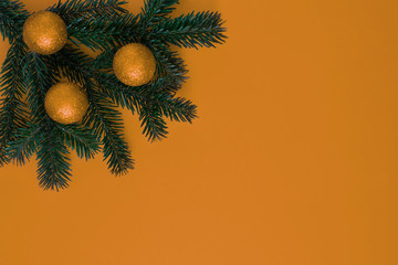 A green Christmas tree branch with toy balls on an orange background in the corner of the frame.