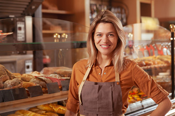 Lovely mature small business owner smiling to the camera at her bakery store, copy space