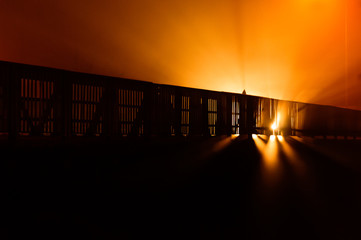 At night, a passing car crosses the bridge railing with lights.