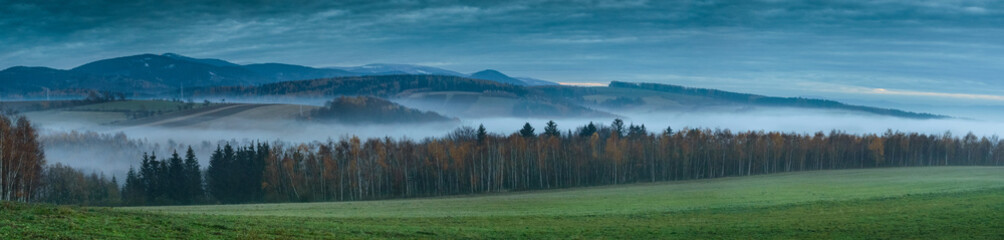 Panorama of the Sudetes mountains after sunset, flowing fog in the valleys.