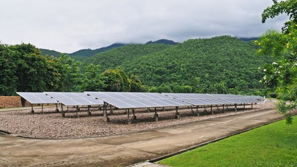 Fototapeta premium Solar panels / solar farm with trees and mountains / hills background, selective focus at the panels.