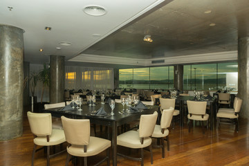 Luxurious party room with various tables, plates, cutlery and wine glasses. Windows overlooking the sea and sunset. Hall for events, parties, celebrations with beautiful view.