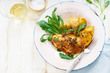 Healthy dinner with roasted chicken, potato wedges on white wooden table