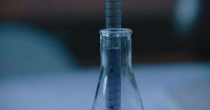 Scientist taking out a purple liquid from a conical flask to test chemicals for reactions in a lab. Close up, handheld, slow motion, tracking, shot with BMPCC 4K. Concept: science, chemistry