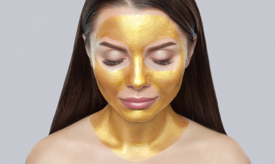 Portrait of a brunette woman who makes a golden mask on her face, neck and collarbones against...