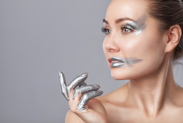 Portrait of a beautiful happy woman with beautiful creative makeup in silver colors. Fingers in silver paint. Make-up concept.