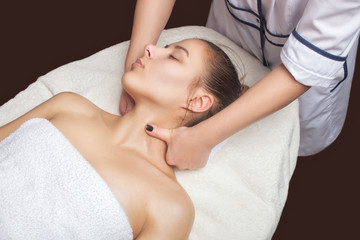 Fototapeta na wymiar Masseur makes a relaxing massage on the face, neck, shoulders and collarbones of a young beautiful woman in a spa. Cosmetology and massage concept.
