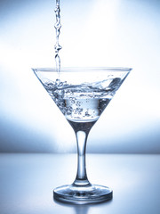 one glass of water with spray from falling water jet, white background, isolated object